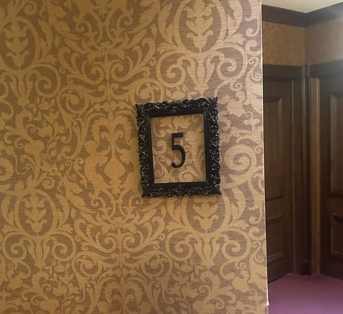 An ornate black frame on Victorian wallpaper holding the number five, marking the Mizpah Hotel fifth floor