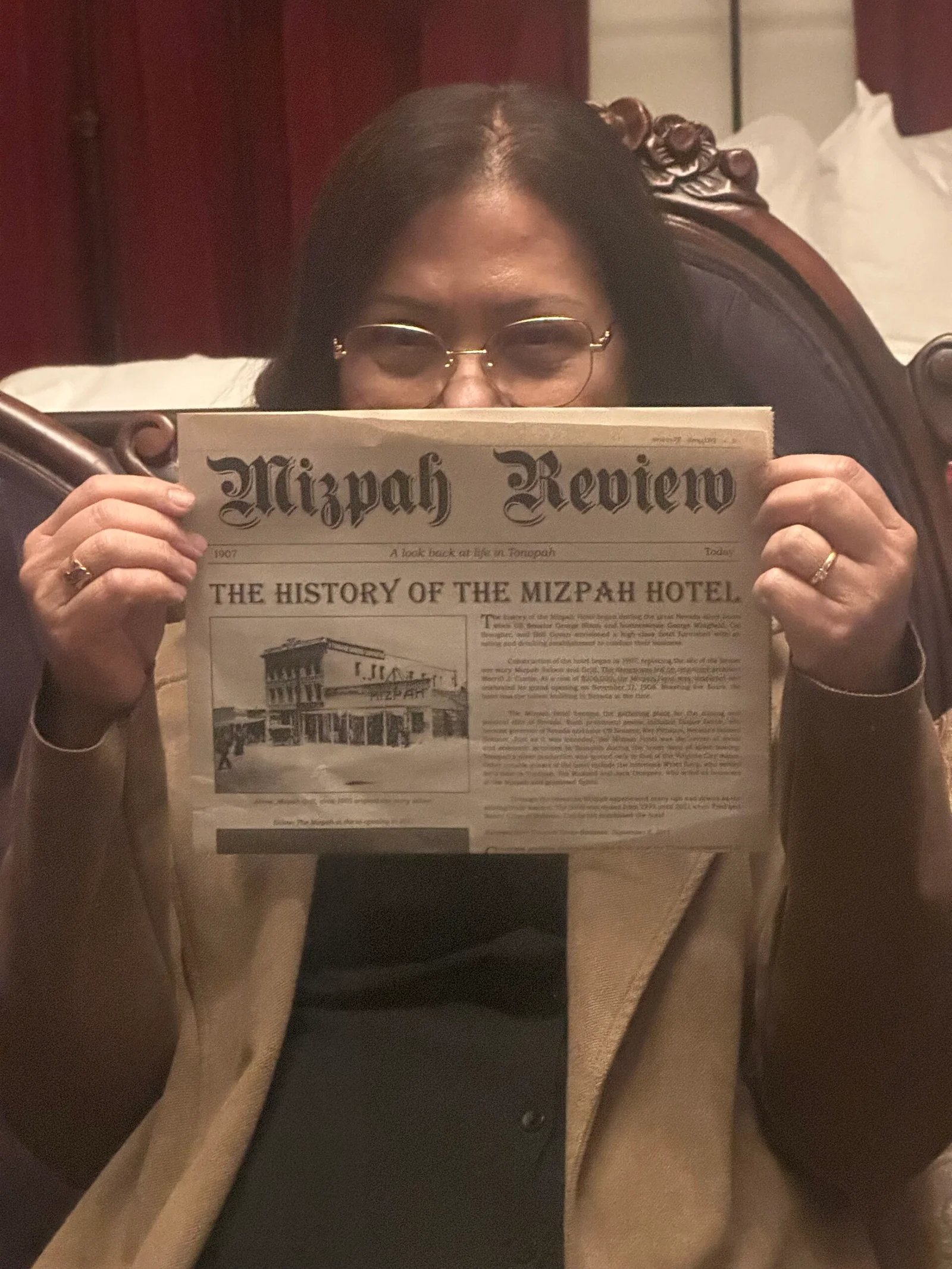 A reader hidden behind a copy of the Mizpah Review newspaper, eyes just visible over the top